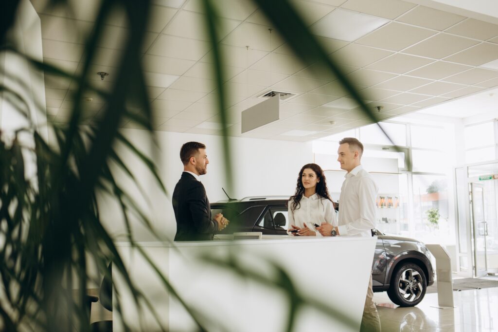 Middle age couple choosing and buying car at car showroom. Car salesman gives them car keys.